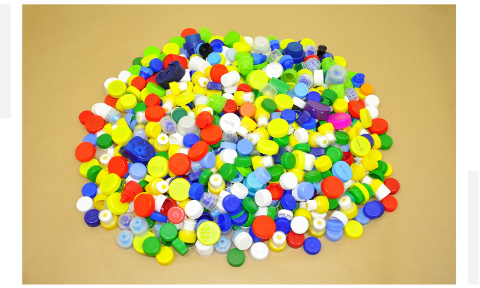 A large pile of colorful plastic bottle caps is spread out on a flat surface.