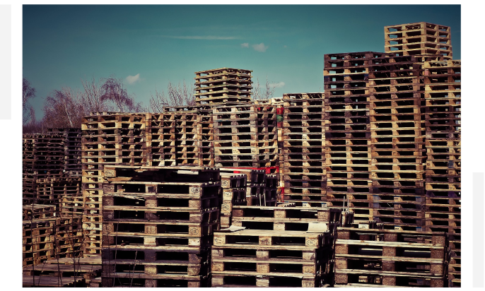 Stacks of wooden pallets piled high against a clear blue sky background.