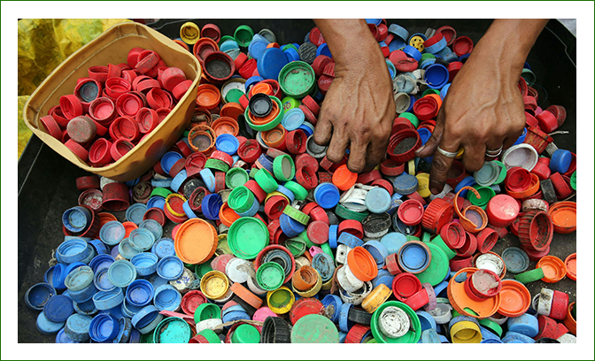 Two hands sorting a large pile of colorful plastic bottle caps, with a container of red caps to the side.